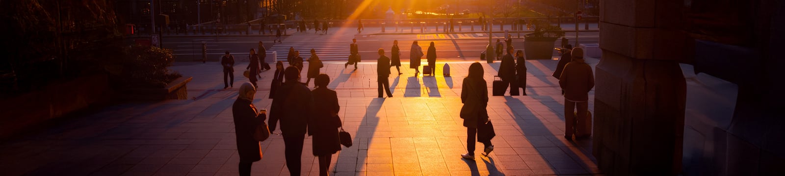 Silhouettes of People Walking Through Grand City Plaza at Dramatic Sunset with Golden Sun Rays